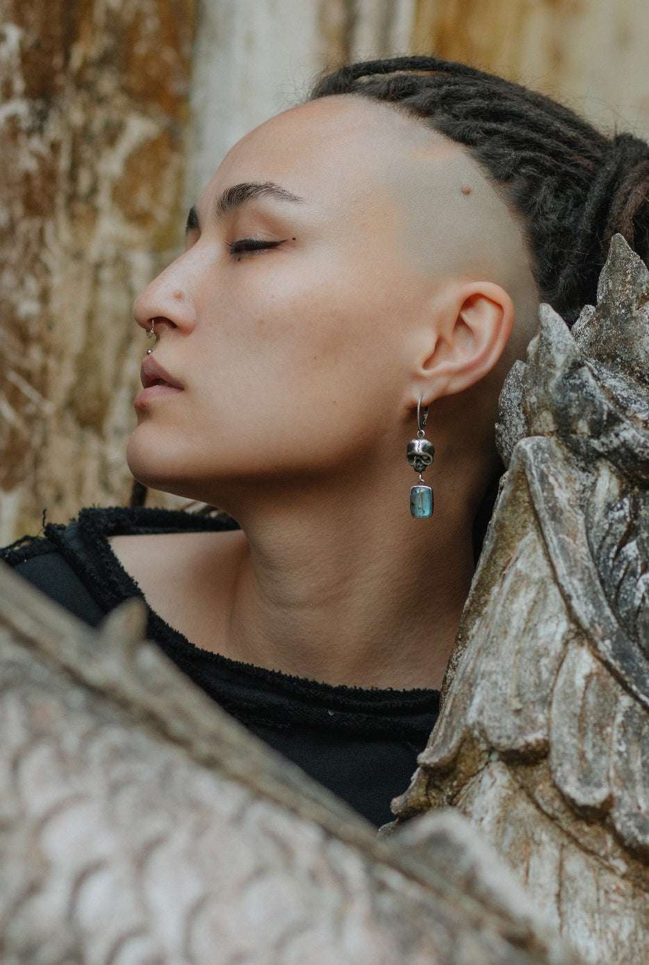 Close-up of handmade oxidised silver Skull earrings with blue gems, worn by a model with dreadlocks and shamanic vibe