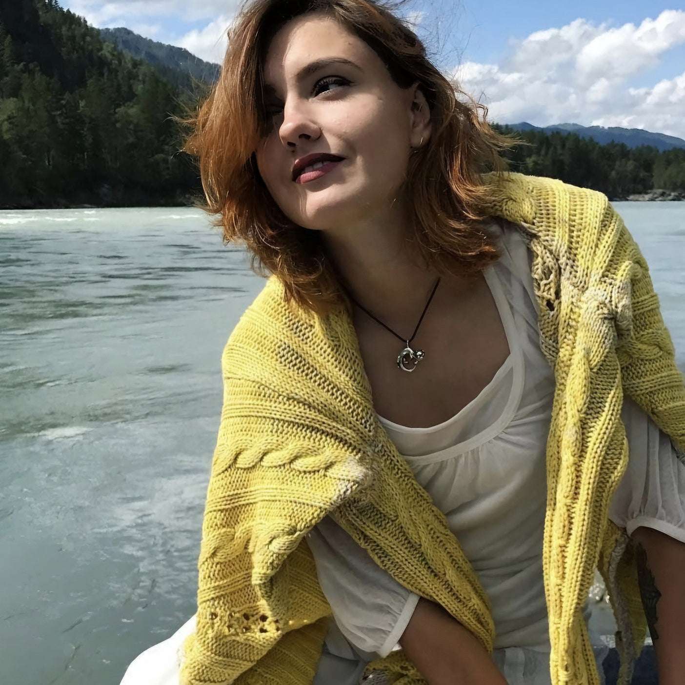 Woman in a yellow shawl smiling outdoors near a lake, wearing the silver Otter necklace as part of a relaxed, joyful outfit.