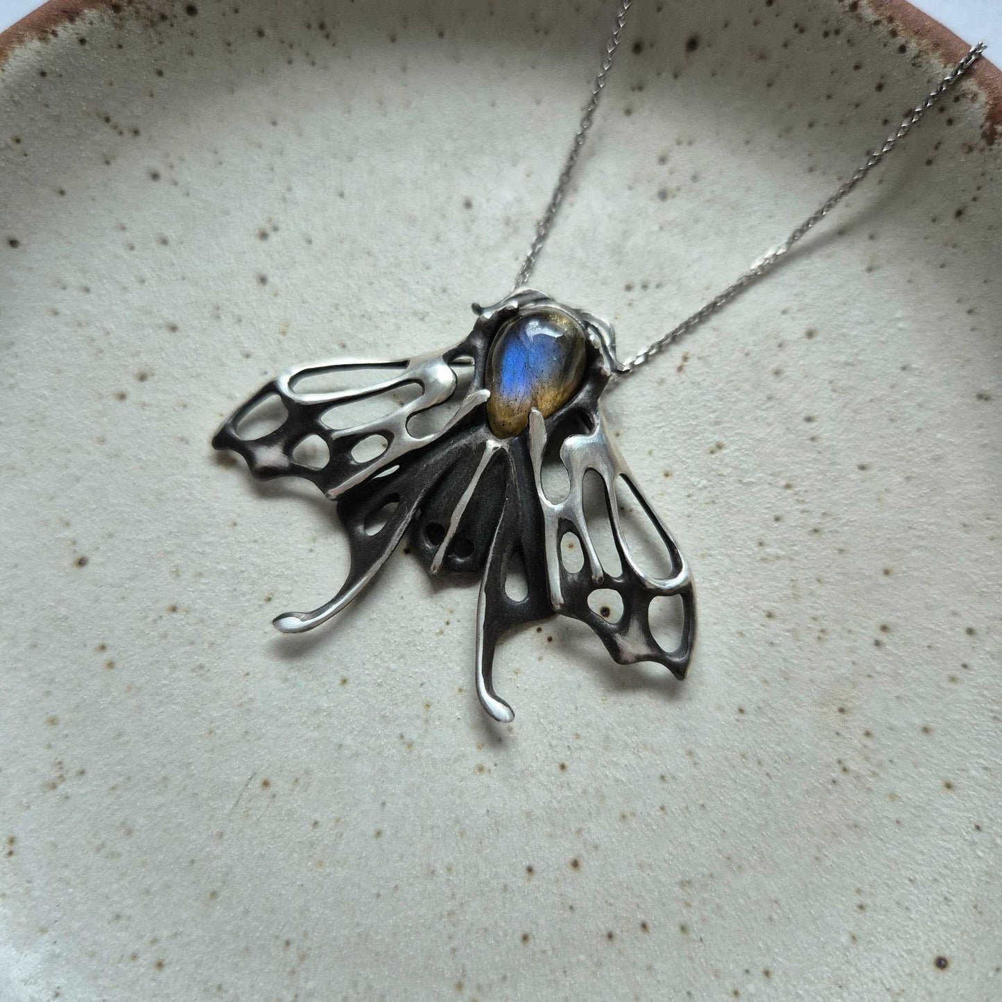 Sculptural silver Moth necklace with blue labradorite, laid on pale ceramic