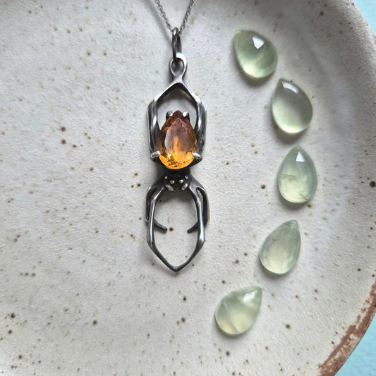 Silver spider necklace with citrine, styled on a ceramic plate with green teardrop beads