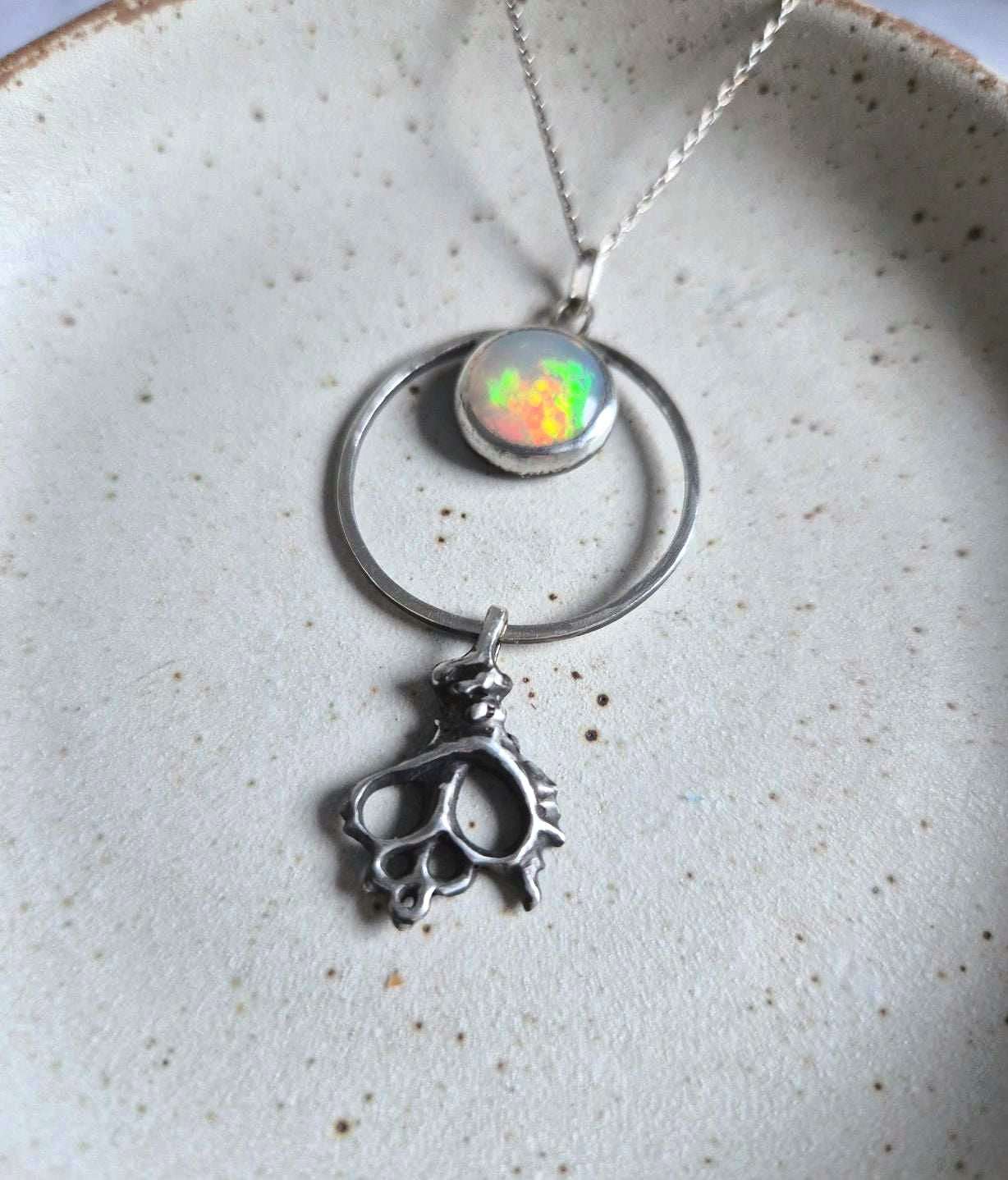 Silver opal necklace with shell charm on ceramic plate — glowing multicolor opal in a circular pendant