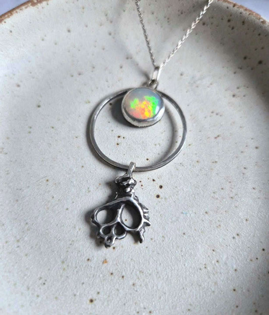 Silver opal necklace with shell charm on ceramic plate — glowing multicolor opal in a circular pendant