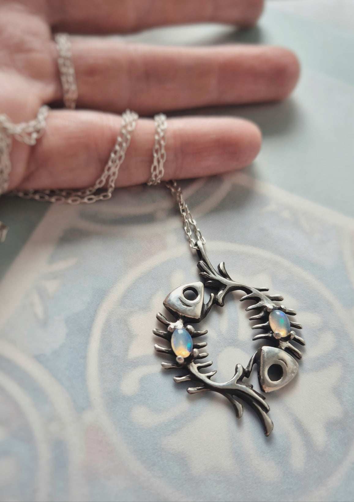 Fish bones necklace with opal cabochons, arranged in a circular shape on soft background