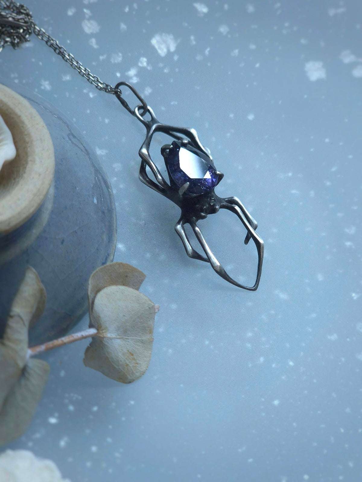 Nature-inspired spider necklace resting on glass surface