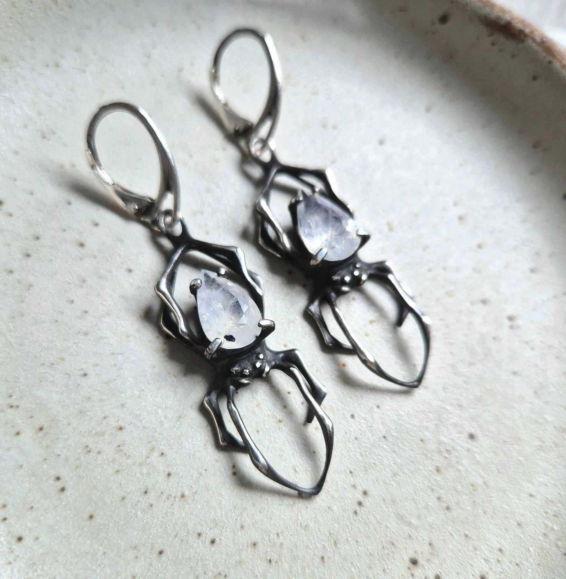 Silver Spider earrings with faceted rainbow moonstones, displayed on ceramic background