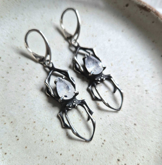Silver Spider earrings with faceted rainbow moonstones, displayed on ceramic background