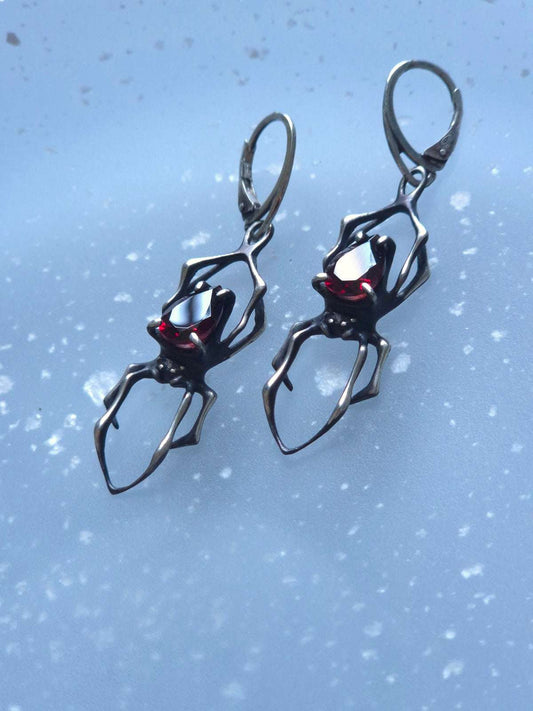 Close-up of handmade oxidised silver spider earrings with natural garnet gemstones