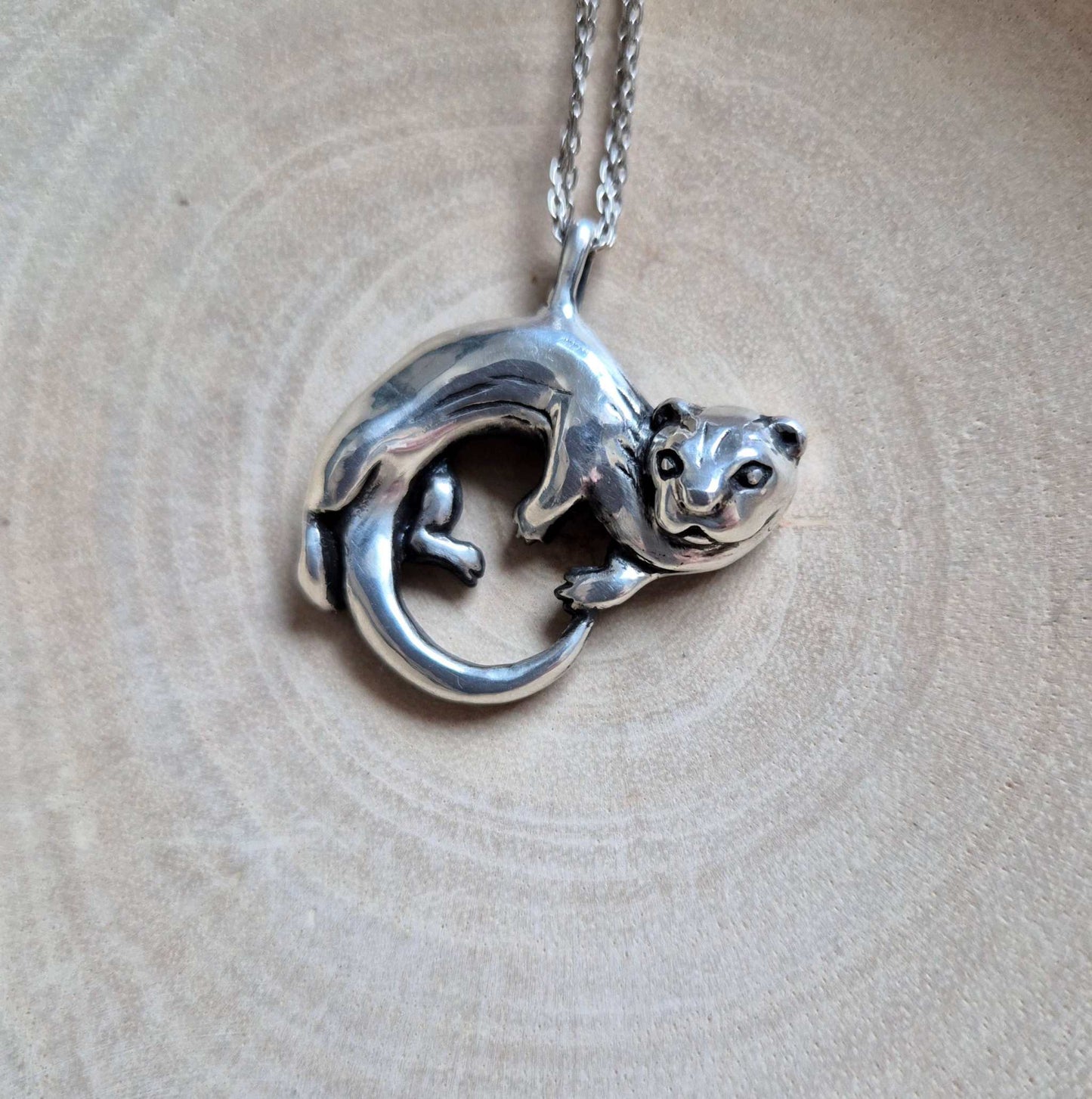 Top view of the silver Otter necklace showing the otter figure curled into a loop, resting on a light surface.