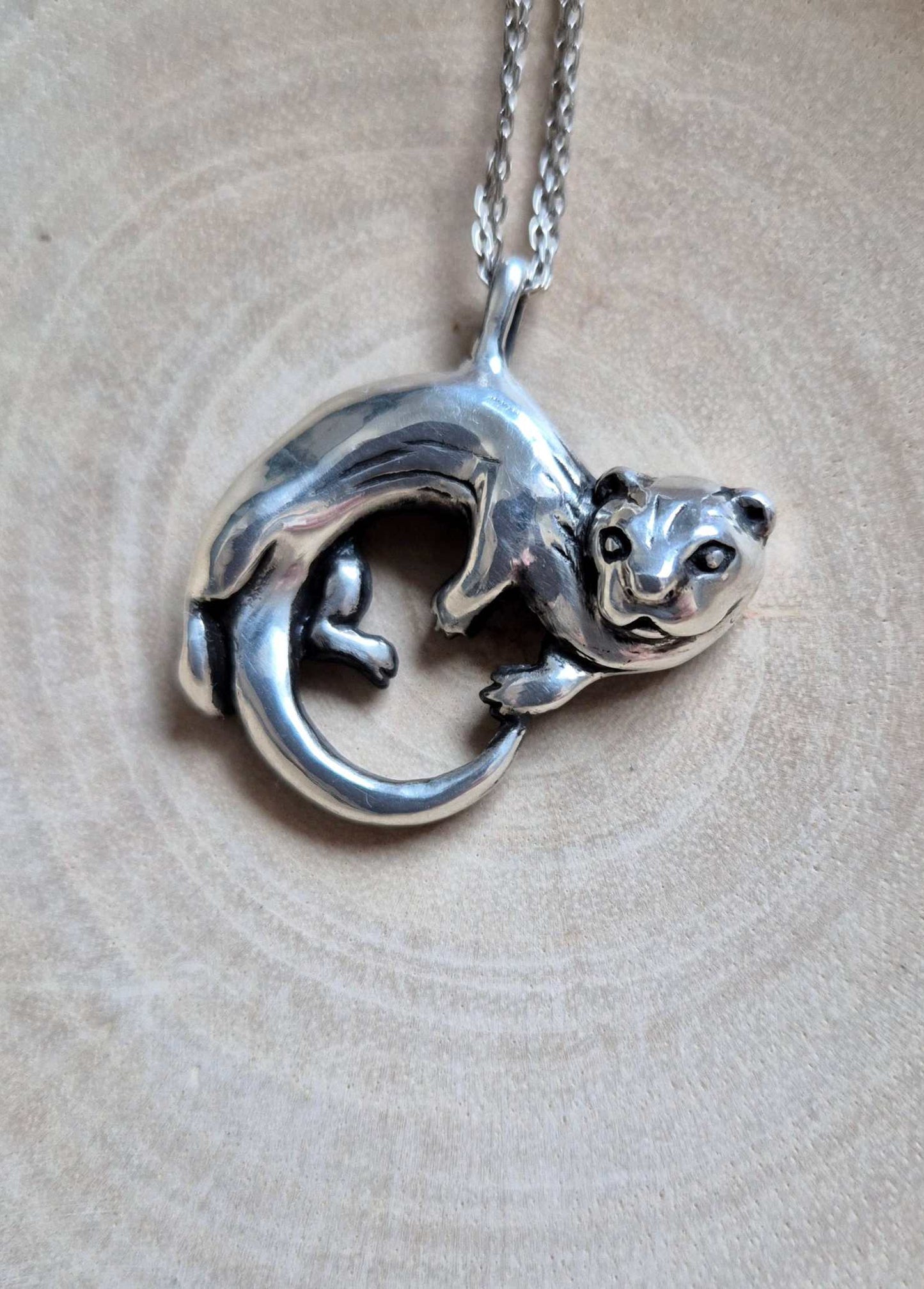 Top view of the curled silver otter pendant and chain on a pale circular-patterned surface