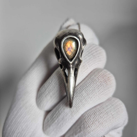 Silver raven skull necklace with golden-flash labradorite held in white glove, front view