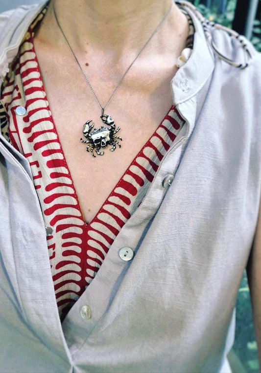 Silver crab skull necklace worn at the center of the chest over a red-and-white patterned top