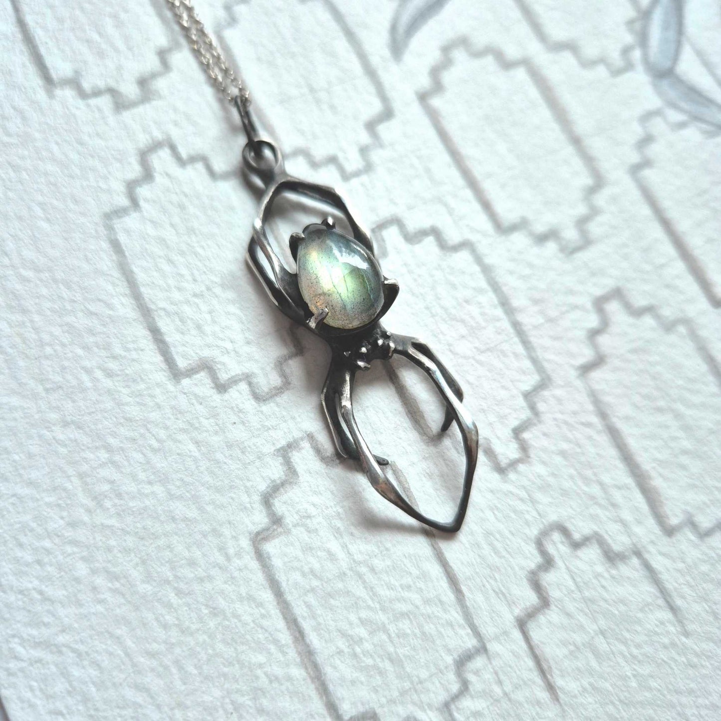 Textured Spider pendant with labradorite, laying flat on patterned background