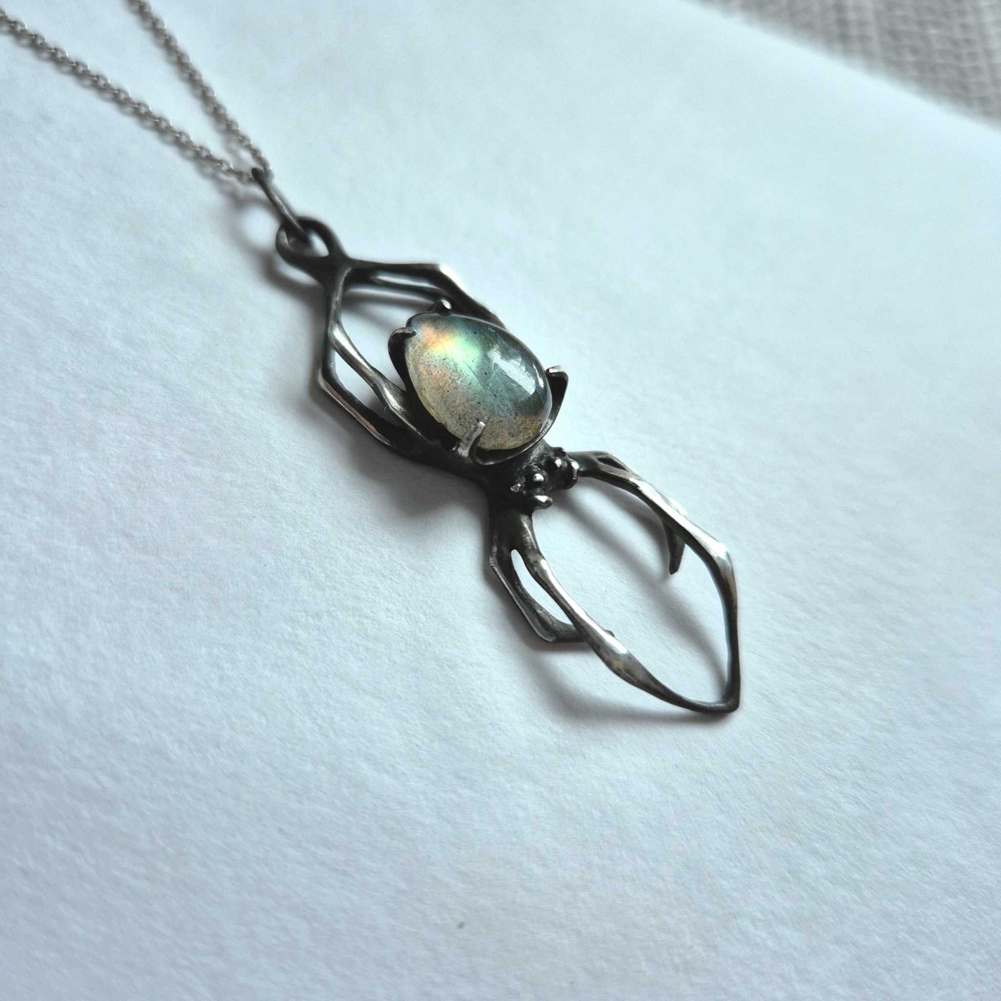 Silver Spider necklace with faceted labradorite gemstone on blue-toned background
