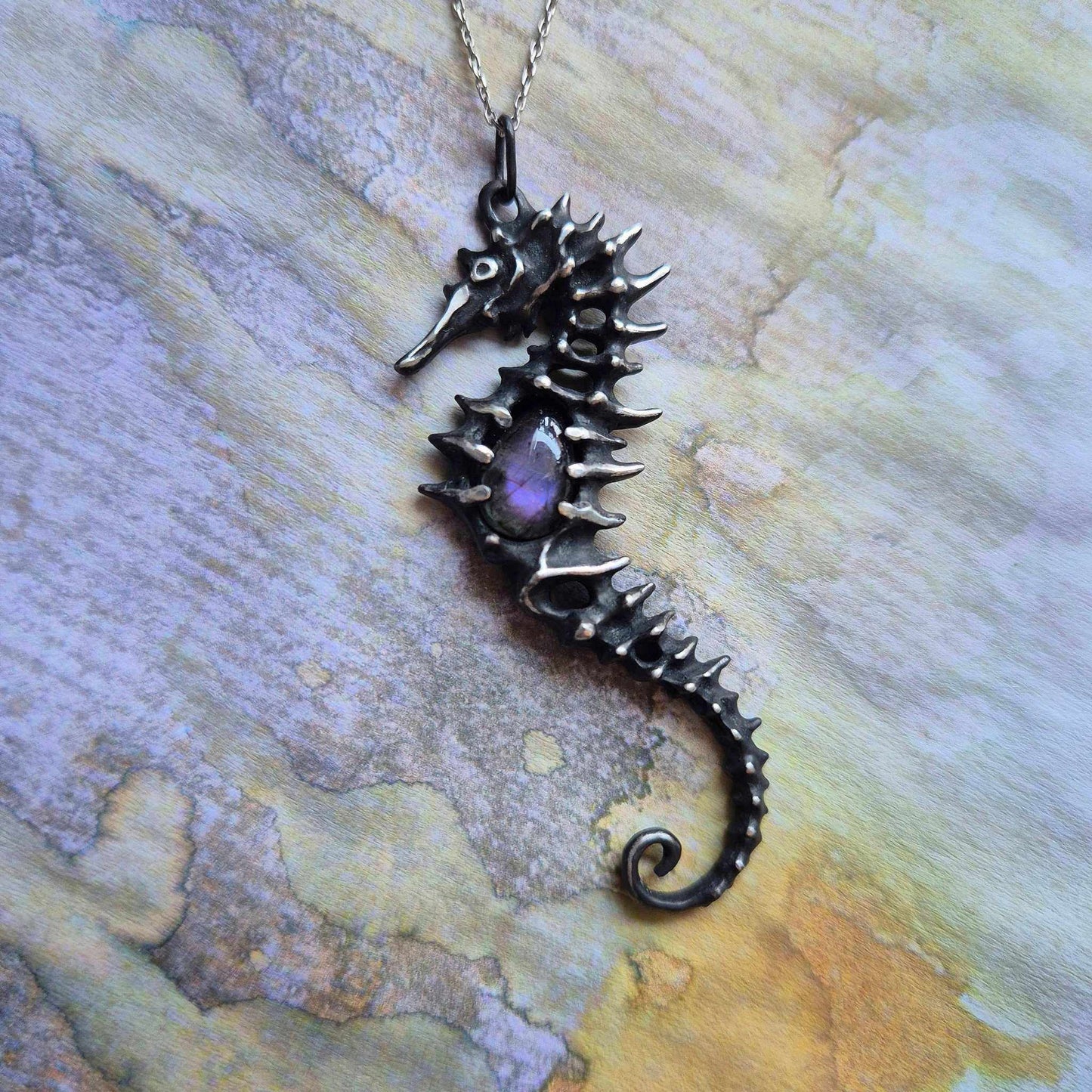 Silver seahorse necklace with purple labradorite displayed on a light purple and yellow paper background