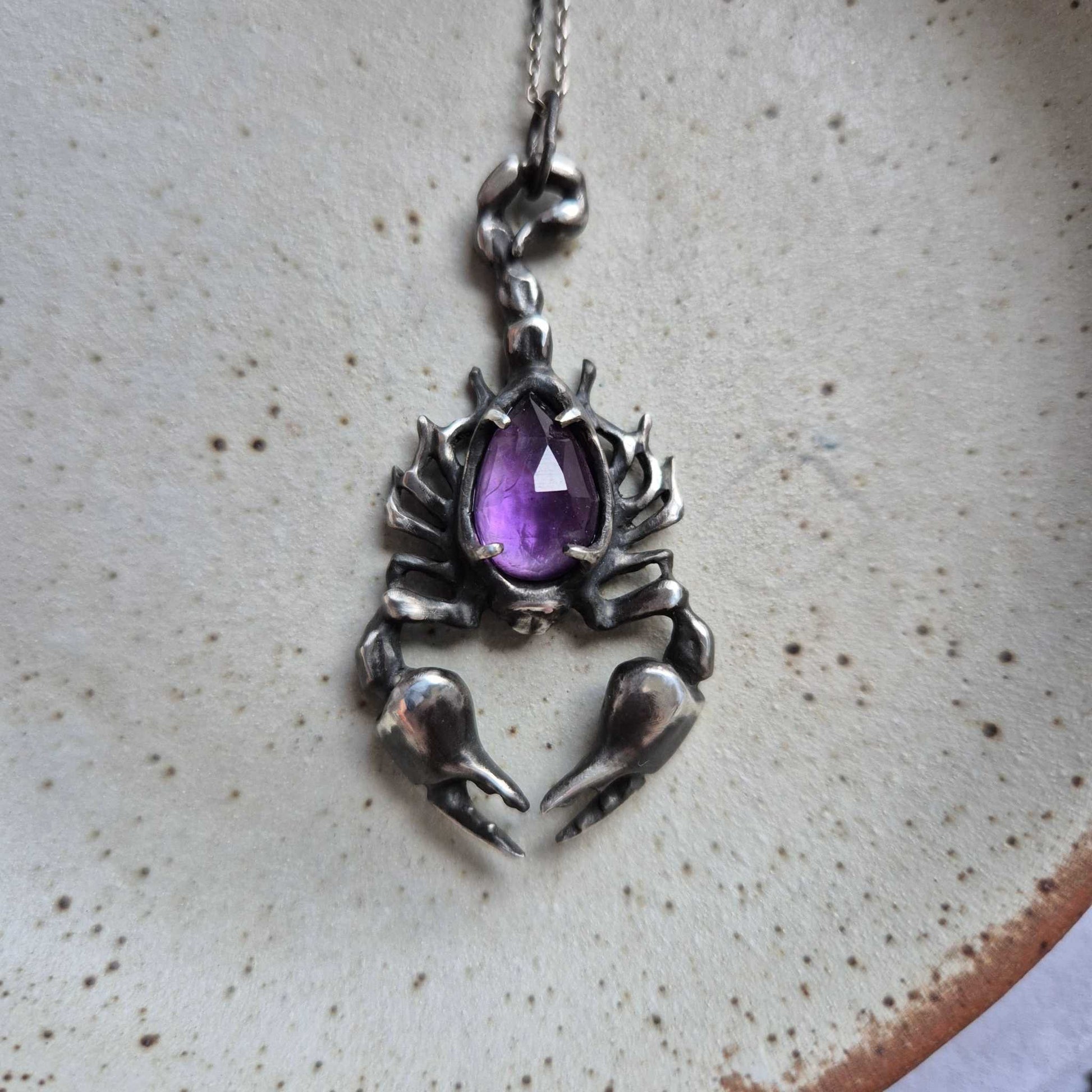 Sculptural silver scorpion pendant with purple rose cut amethyst, styled on textured background