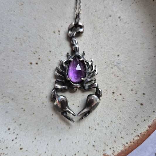 Sculptural silver scorpion pendant with purple rose cut amethyst, styled on textured background