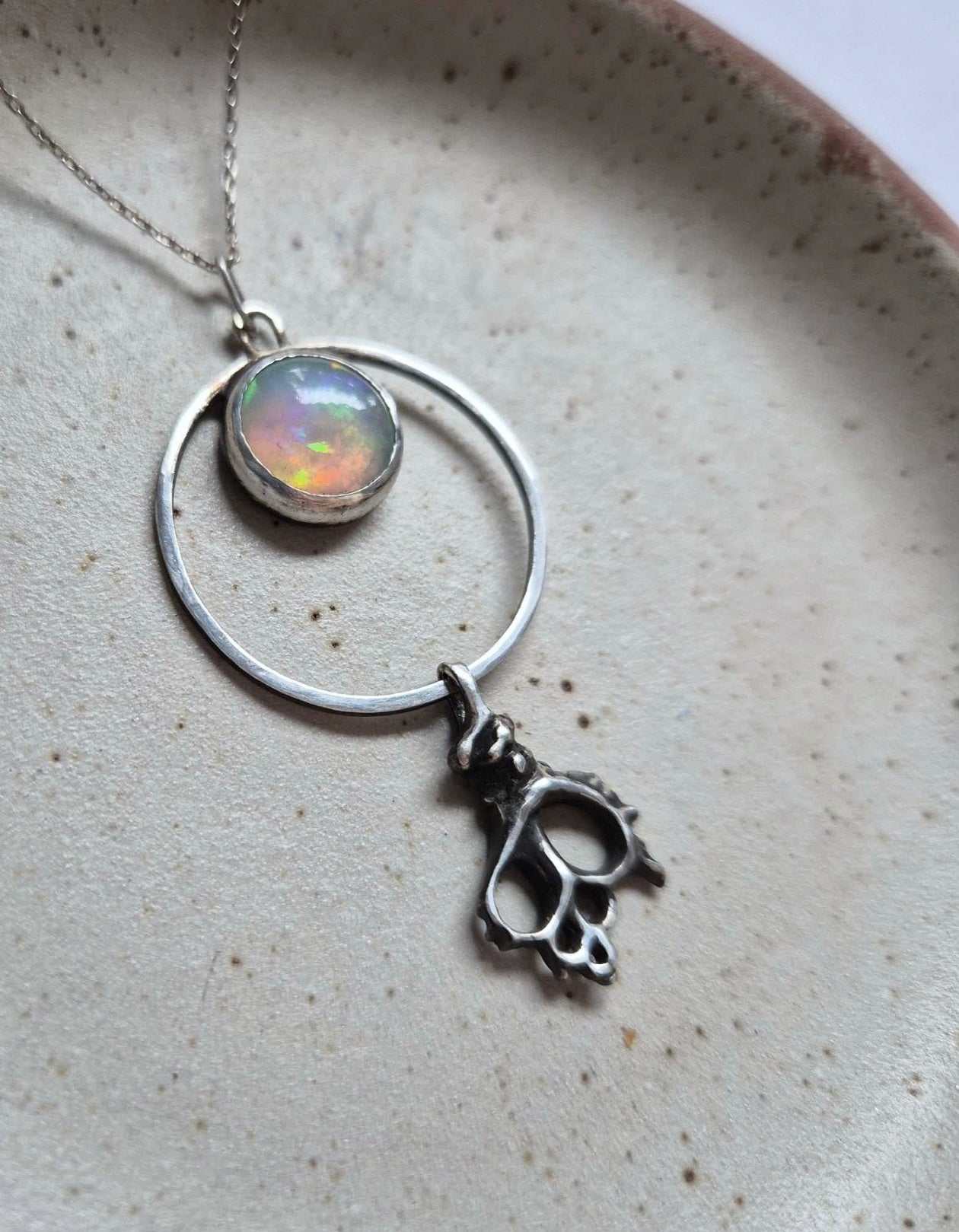 Natural opal and silver shell necklace displayed flat on textured surface — soft fire and motion
