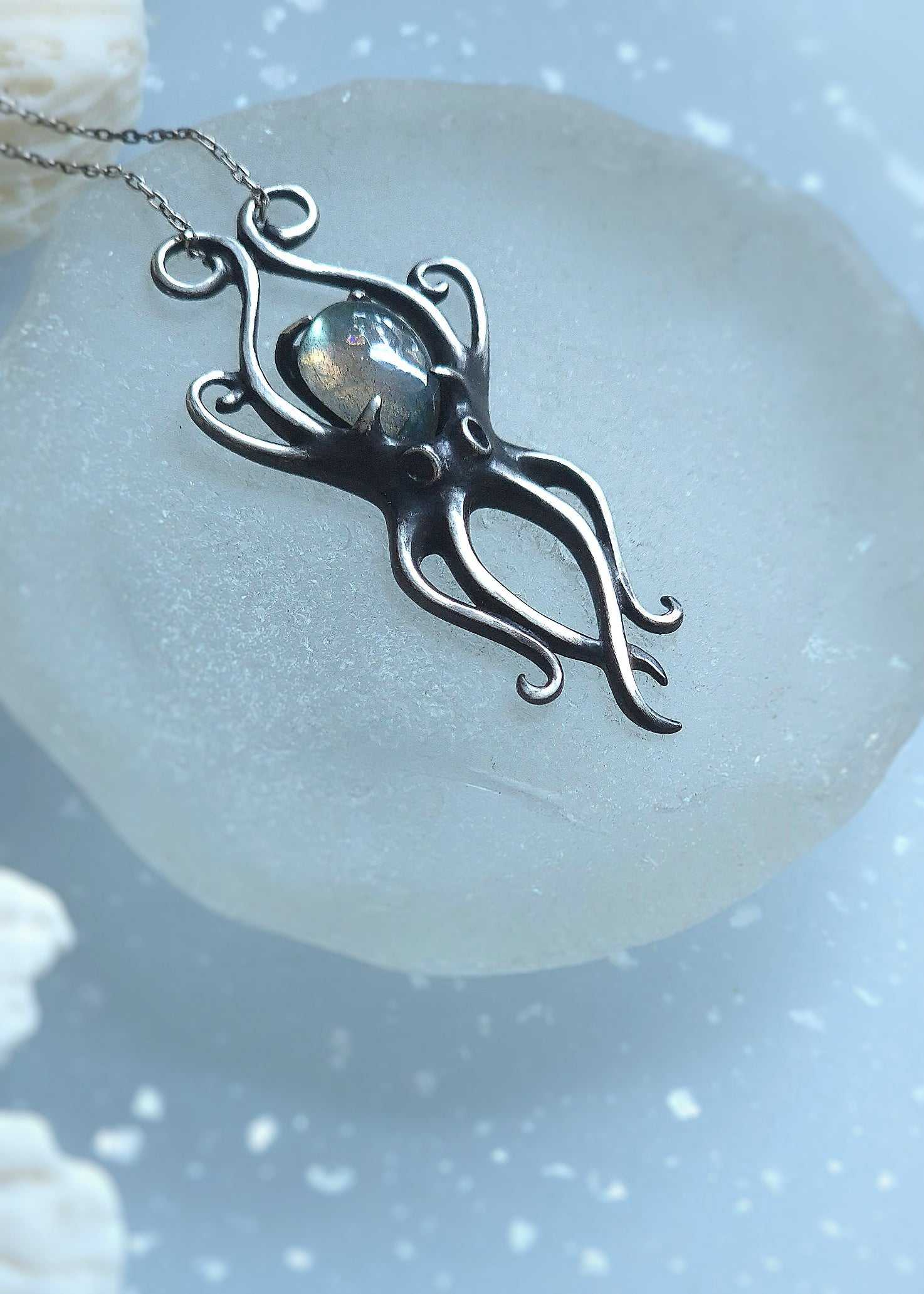 Silver octopus pendant resting on frosted round surface, surrounded by natural white coral
