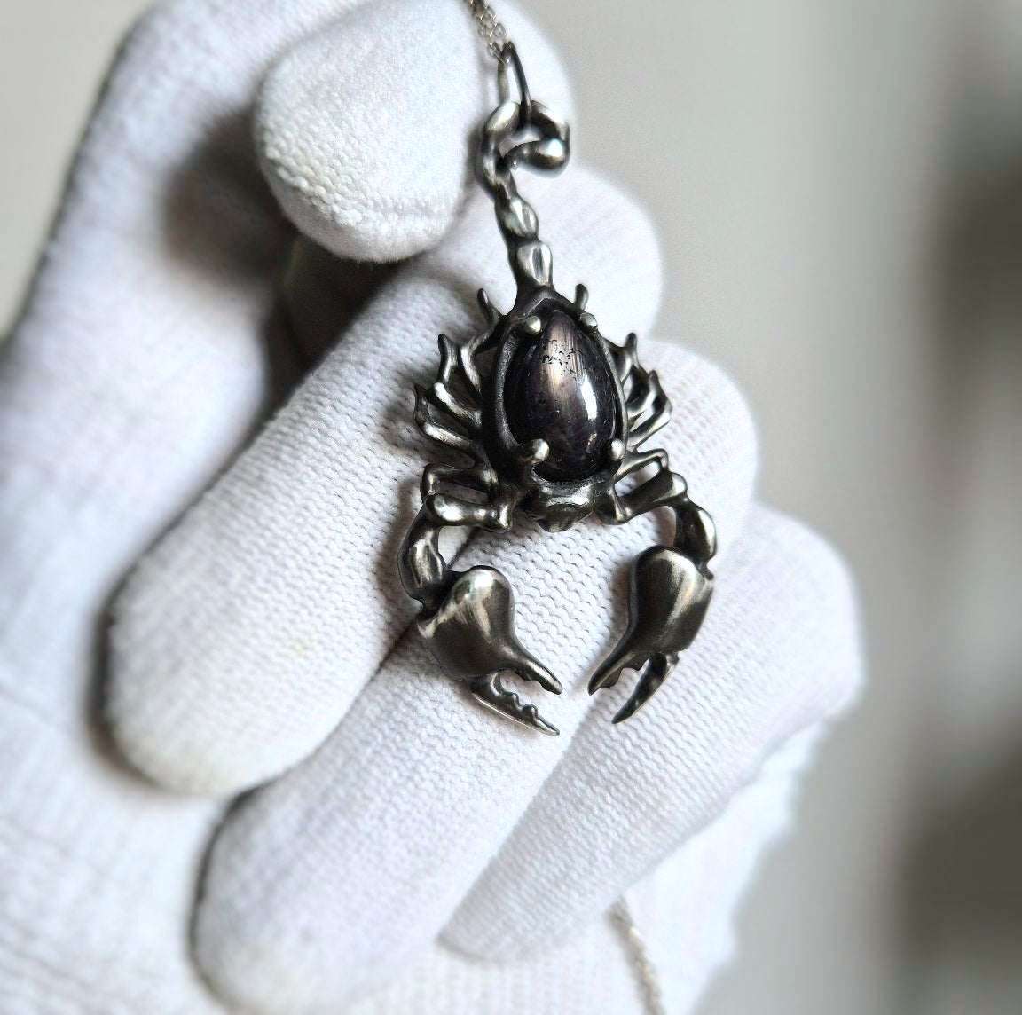 silver Scorpion pendant held in a gloved hand, showcasing details of the silver talisman with a black gem