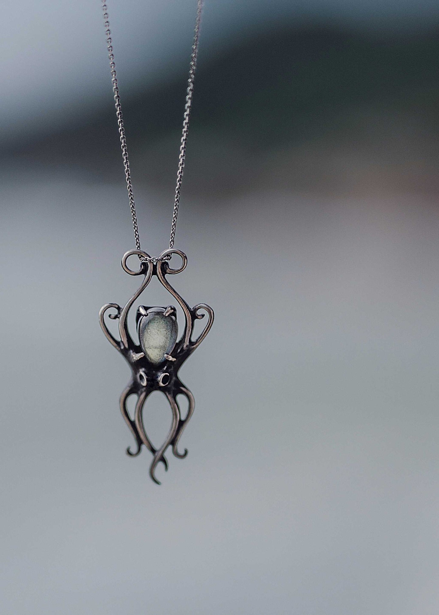 Minimalist close-up of silver octopus necklace floating in air, showing elegant design and gemstone