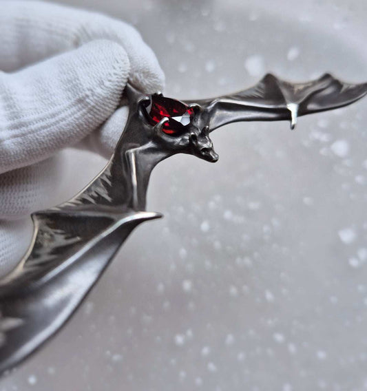 Silver Bat necklace lying on a translucent textured background, showcasing the garnet’s subtle glow