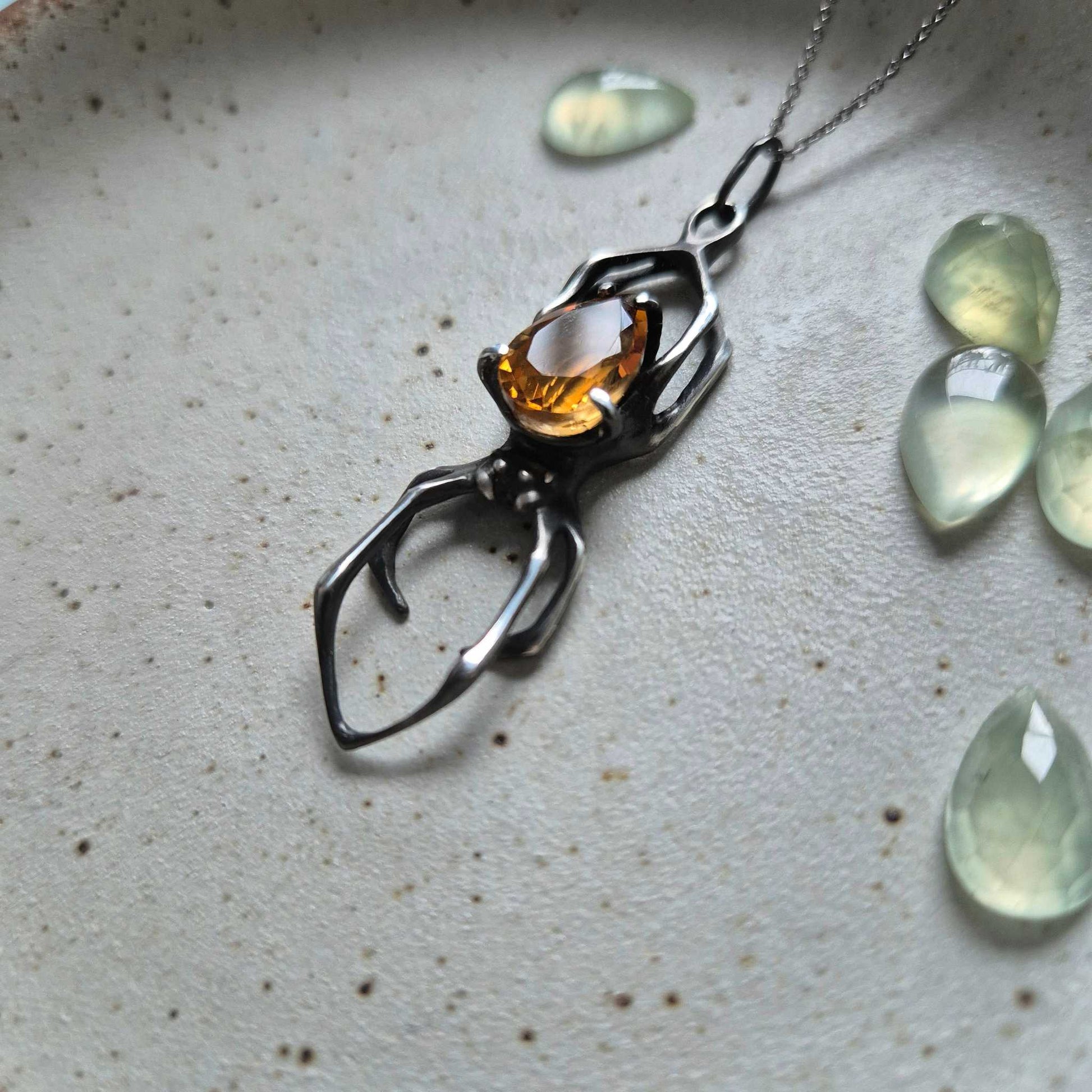 Detailed view of silver spider necklace with natural citrine, styled with curved green glass accents