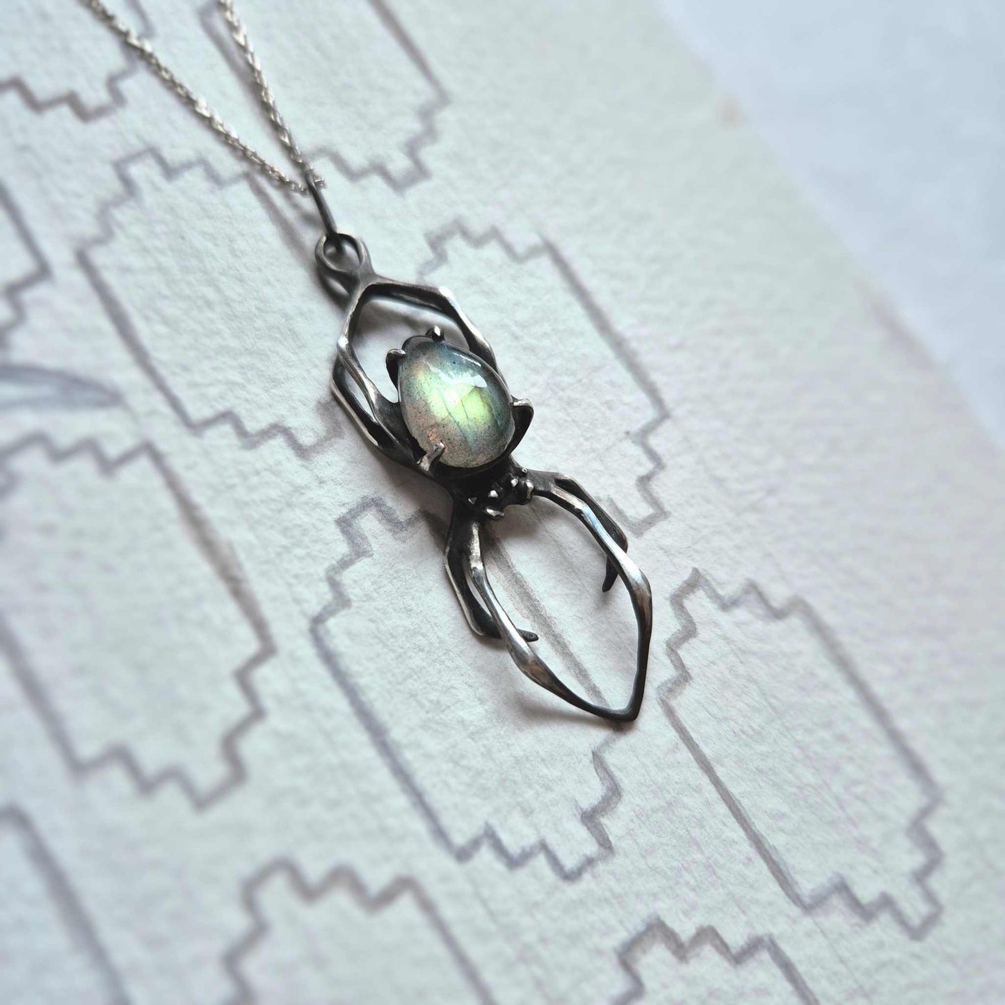 Sterling silver Spider pendant on white patterned surface with glowing labradorite