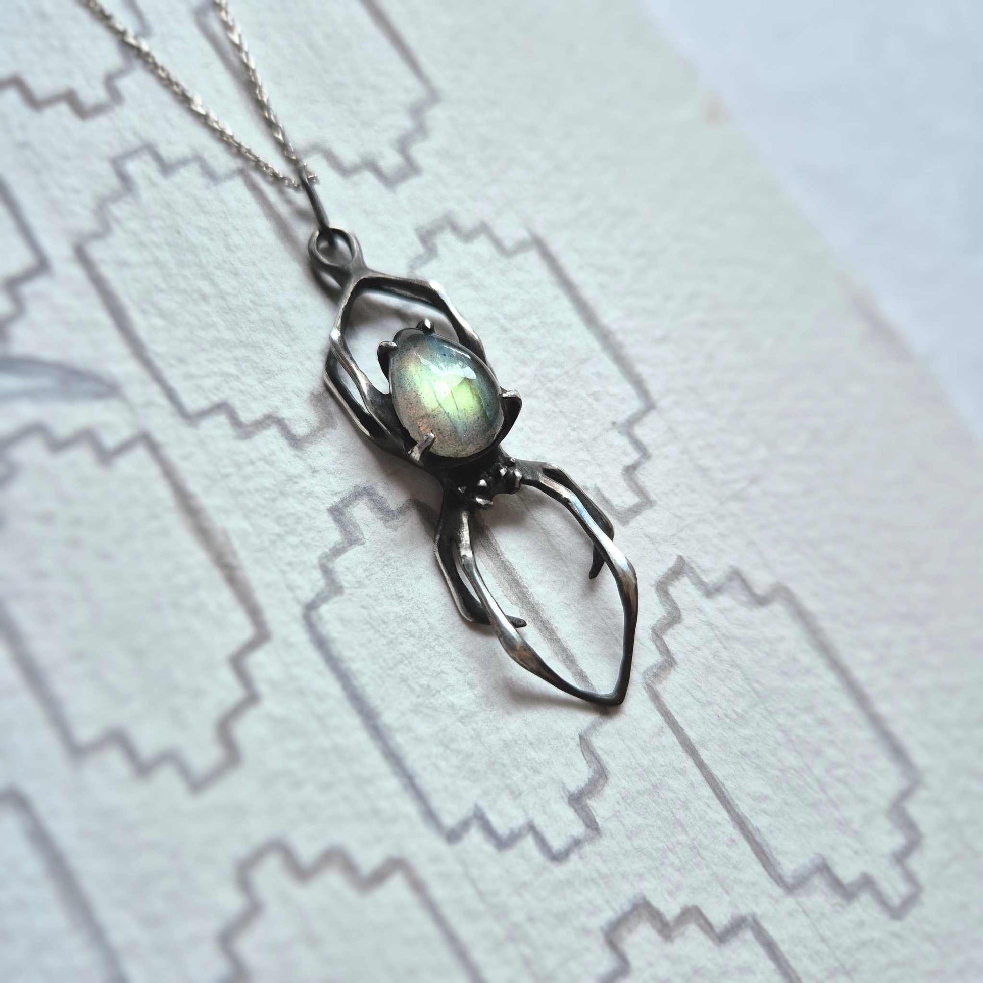 Sterling silver Spider pendant on white patterned surface with glowing labradorite