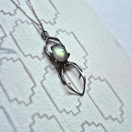 Sterling silver Spider pendant on white patterned surface with glowing labradorite