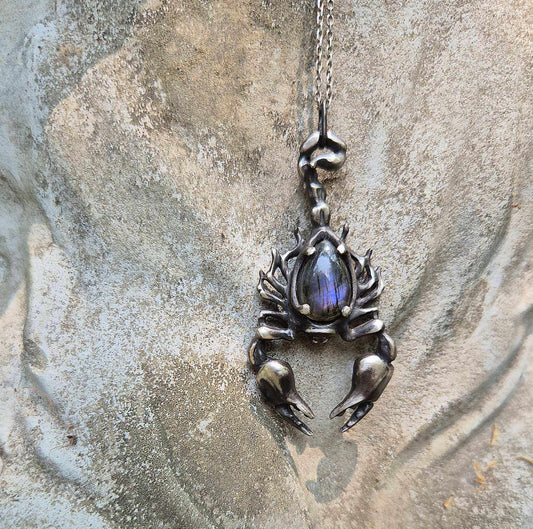 Oxidized silver Scorpion necklace featuring purple labradorite, displayed on rock background