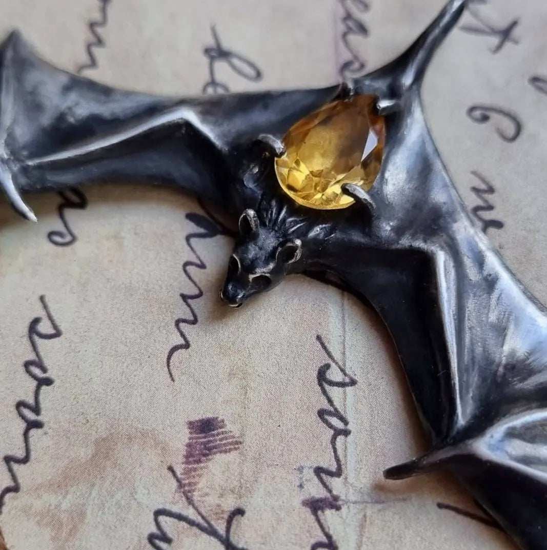 Close-up of silver Bat necklace with citrine gemstone resting on handwritten paper