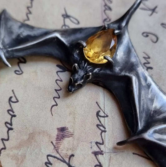 Close-up of silver Bat necklace with citrine gemstone resting on handwritten paper