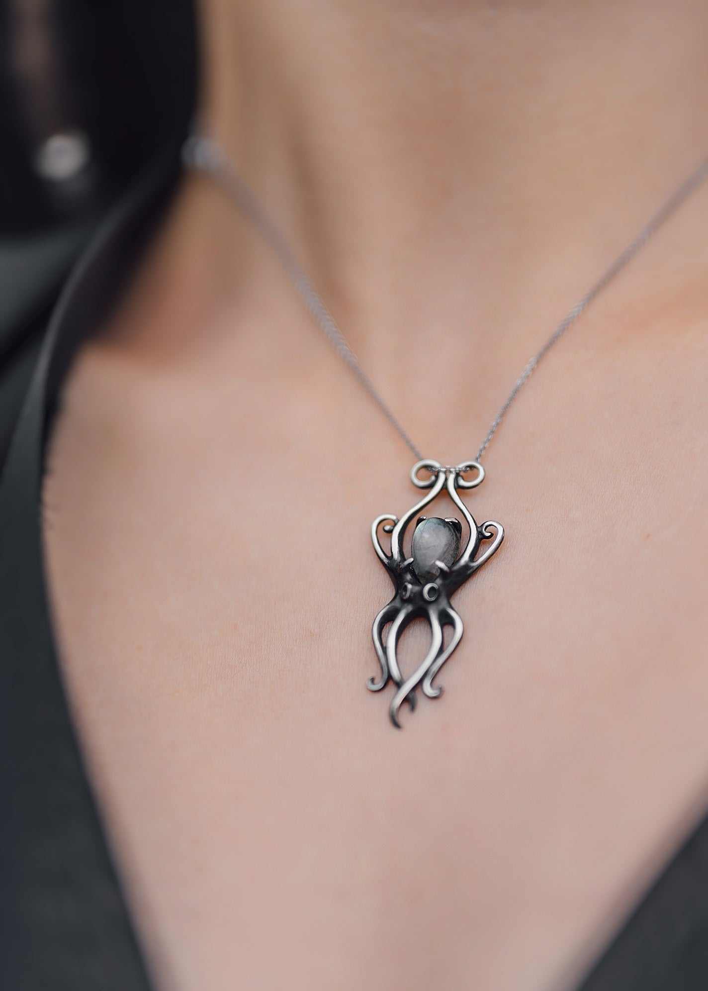 Close-up of silver octopus necklace with curved tentacles and a labradorite gem, on a model