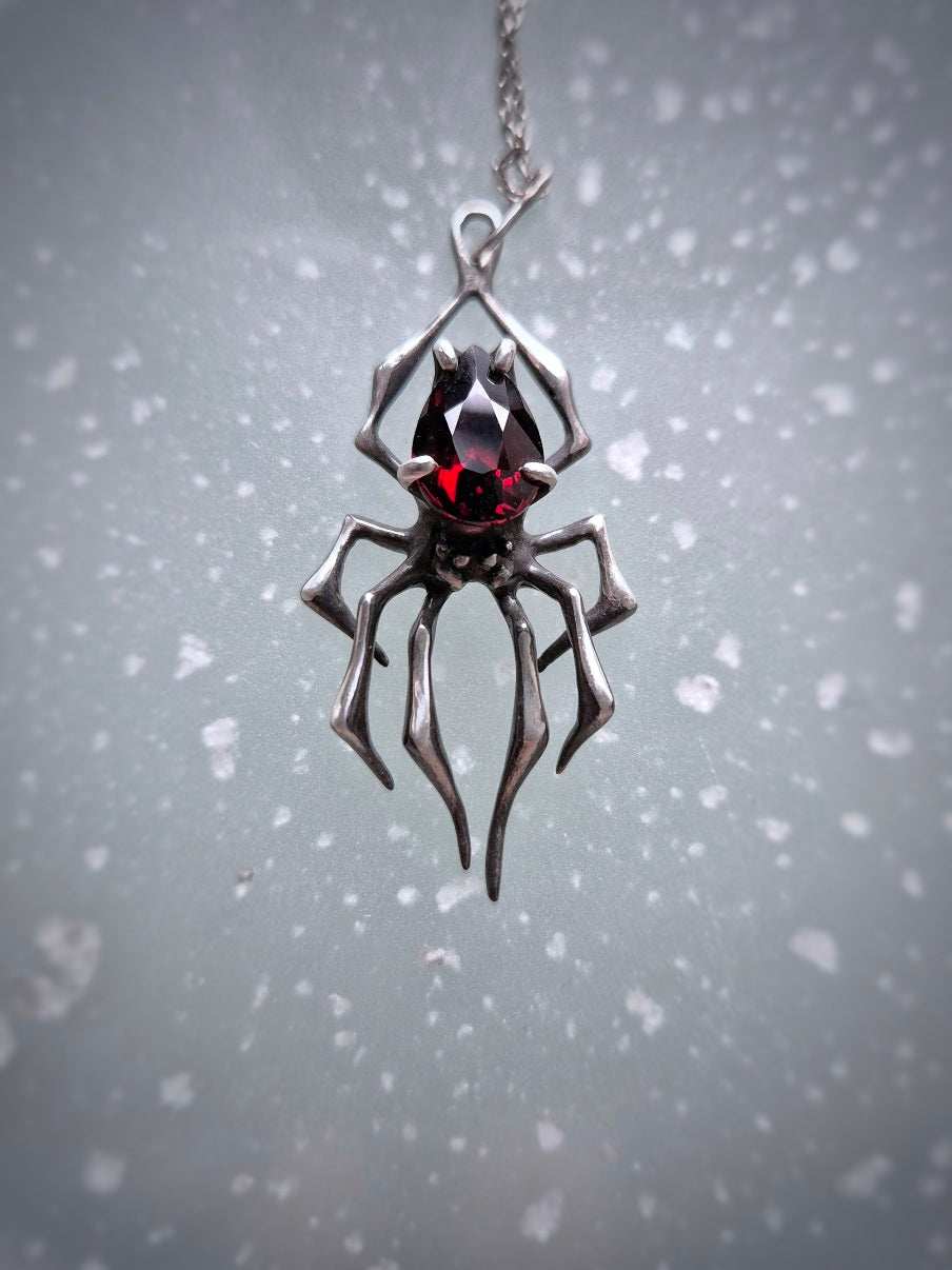 Handmade silver spider necklace with deep-red garnet gemstone on clean background