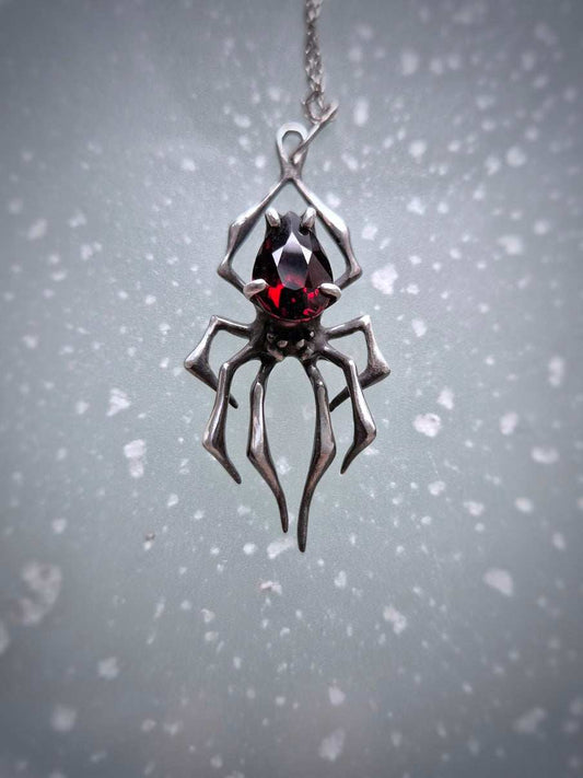 Handmade silver spider necklace with deep-red garnet gemstone on clean background