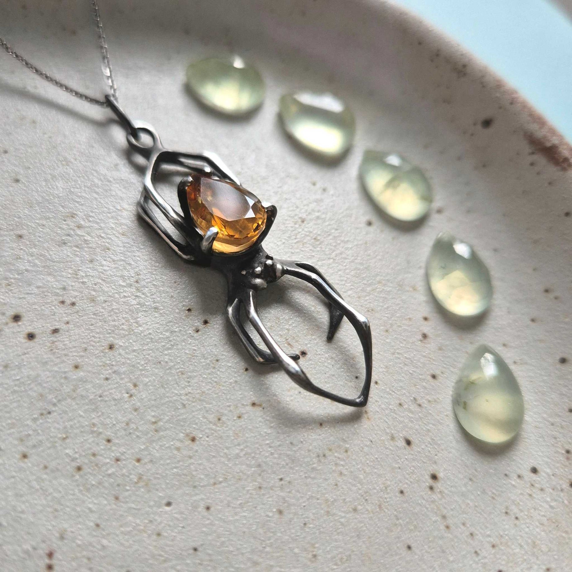 Close-up of oxidized silver spider necklace with warm citrine, surrounded by green beads