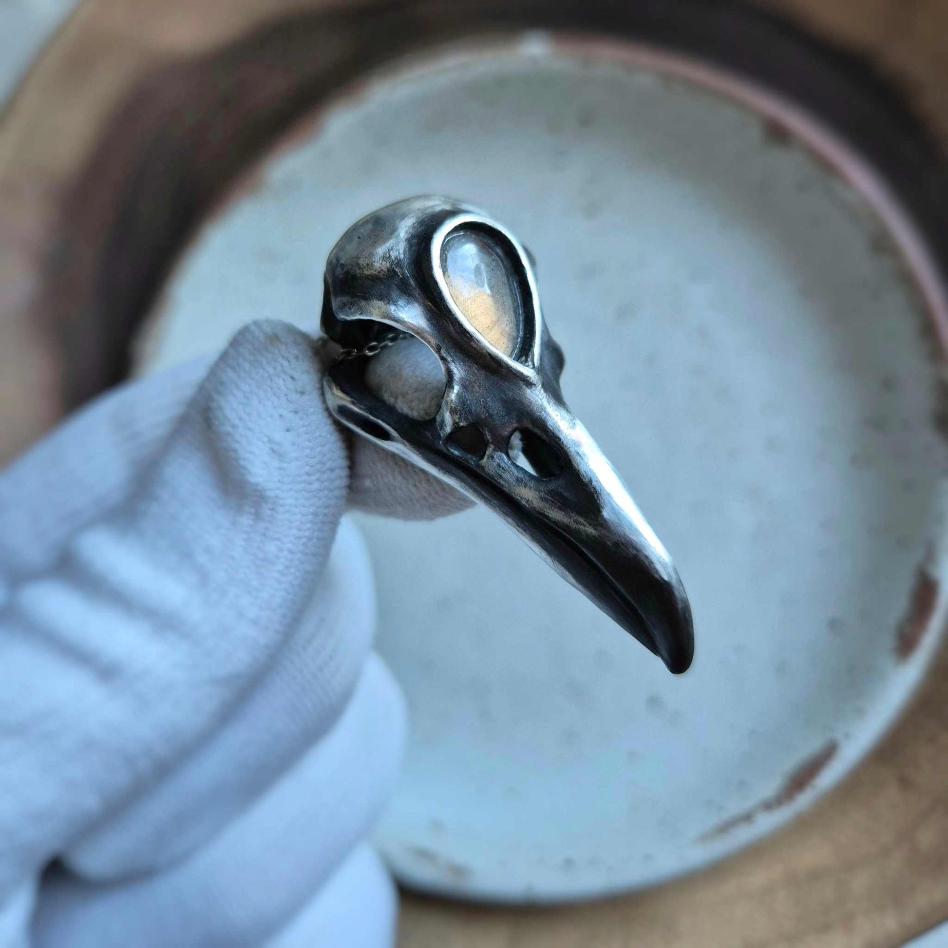 Silver raven skull pendant with golden labradorite gemstone, presented in natural light with texture.