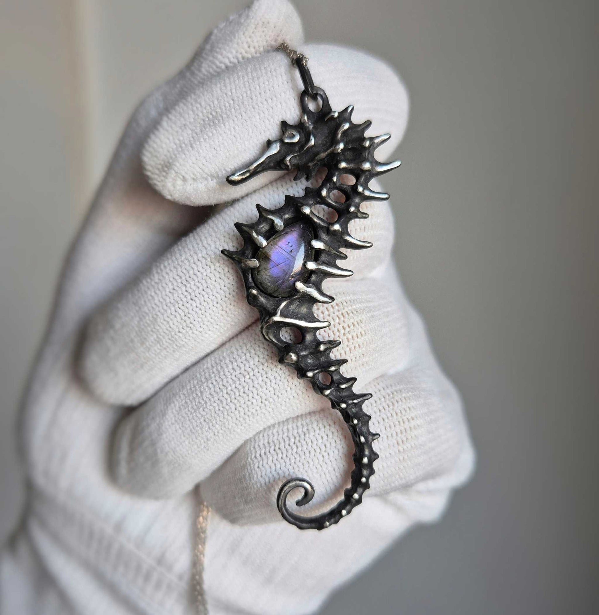 Angled view of the silver seahorse pendant in hand, showcasing the gemstone’s flash and sculptural texture