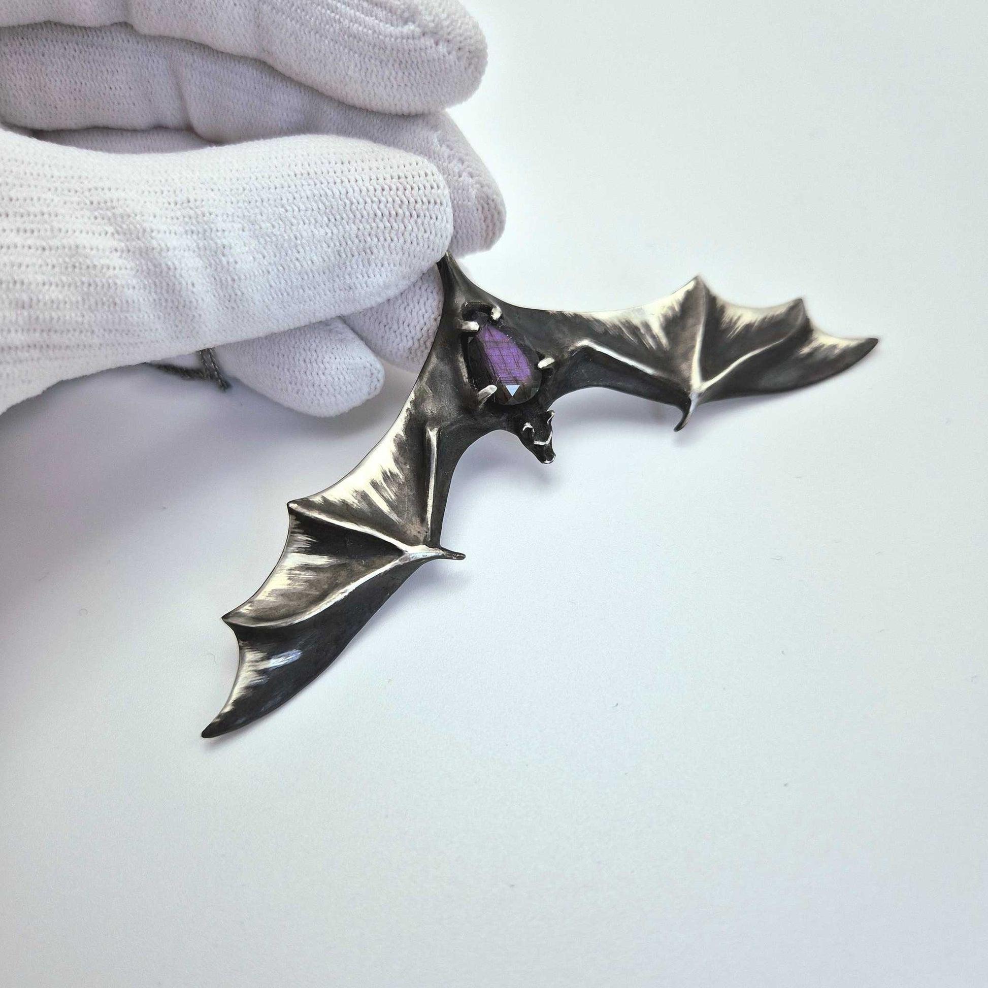 Silver Bat necklace with faceted labradorite gemstone, held in a gloved hand.