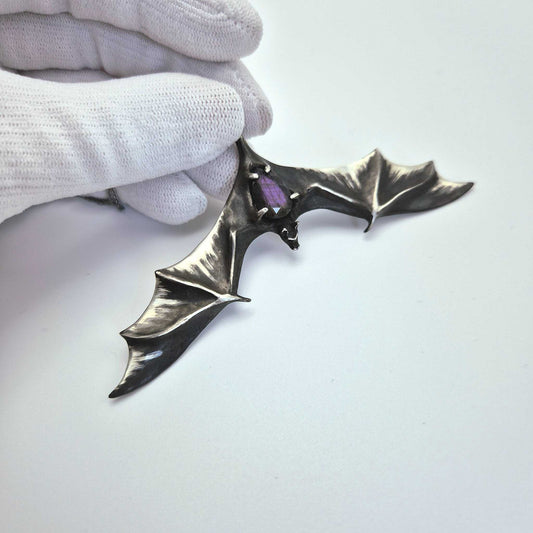 Silver Bat necklace with faceted labradorite gemstone, held in a gloved hand.