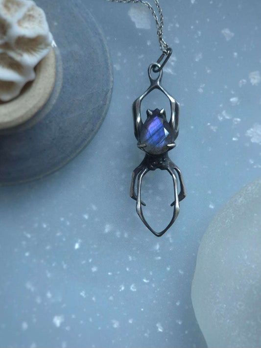 Silver Spider pendant with purple labradorite displayed on a blue speckled background with seashells