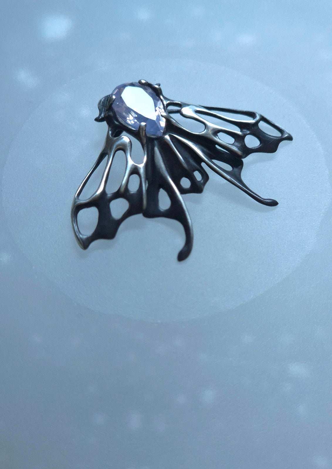 Artistic silver Moth jewelry with semi-transparent lavender quartz on icy-toned surface