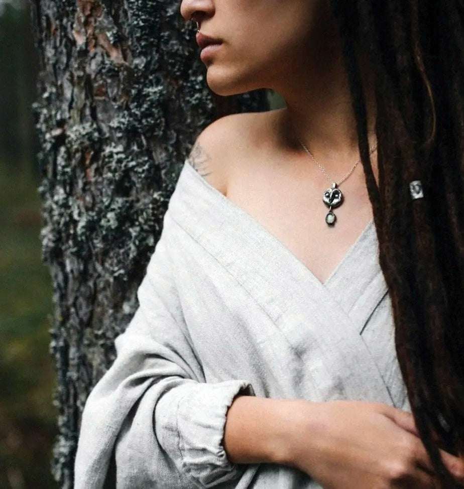 A woman in the forest wearing a silver Owl necklace with a carved Barn owl face and a gem dangle