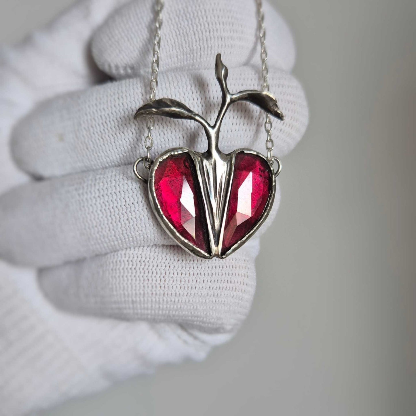 Another gloved hand photo of the Seed Heart necklace, garnets illuminated to show rich crimson tones.