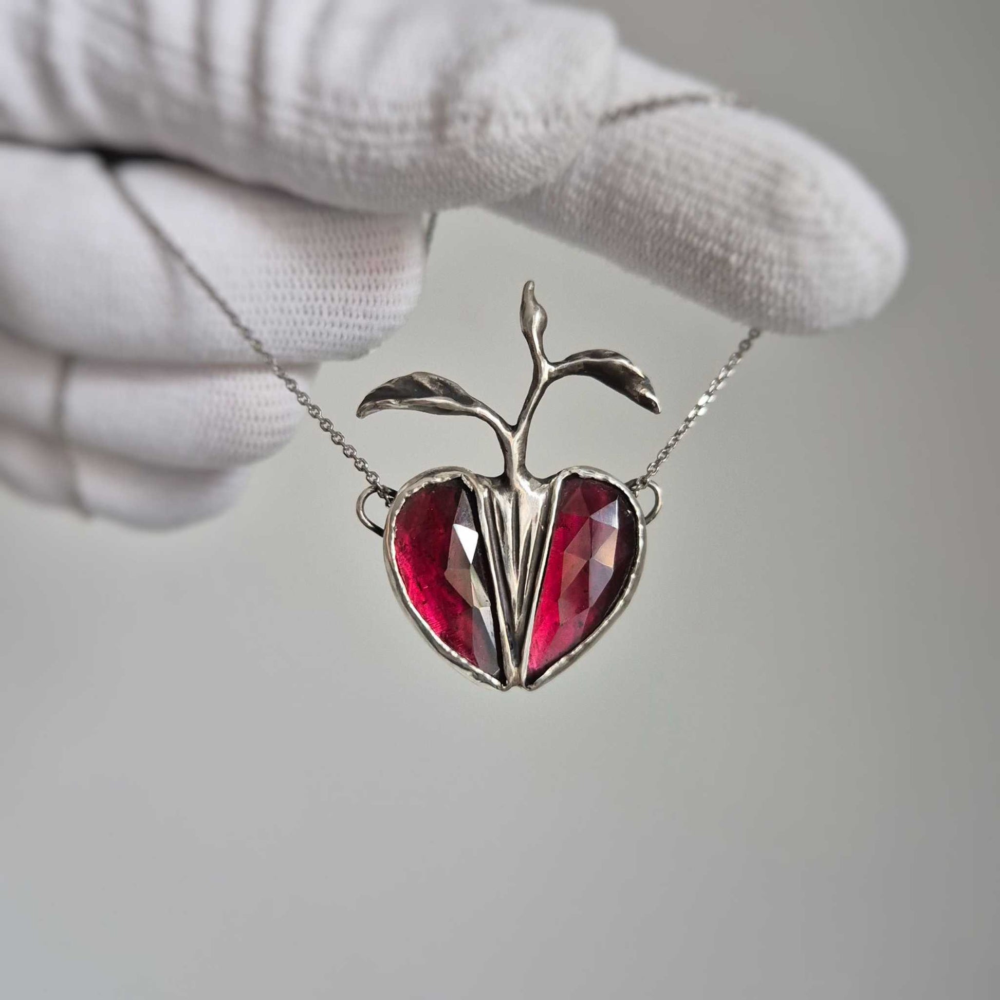 Gloved hand holding the Seed Heart necklace, highlighting the size and handcrafted details.