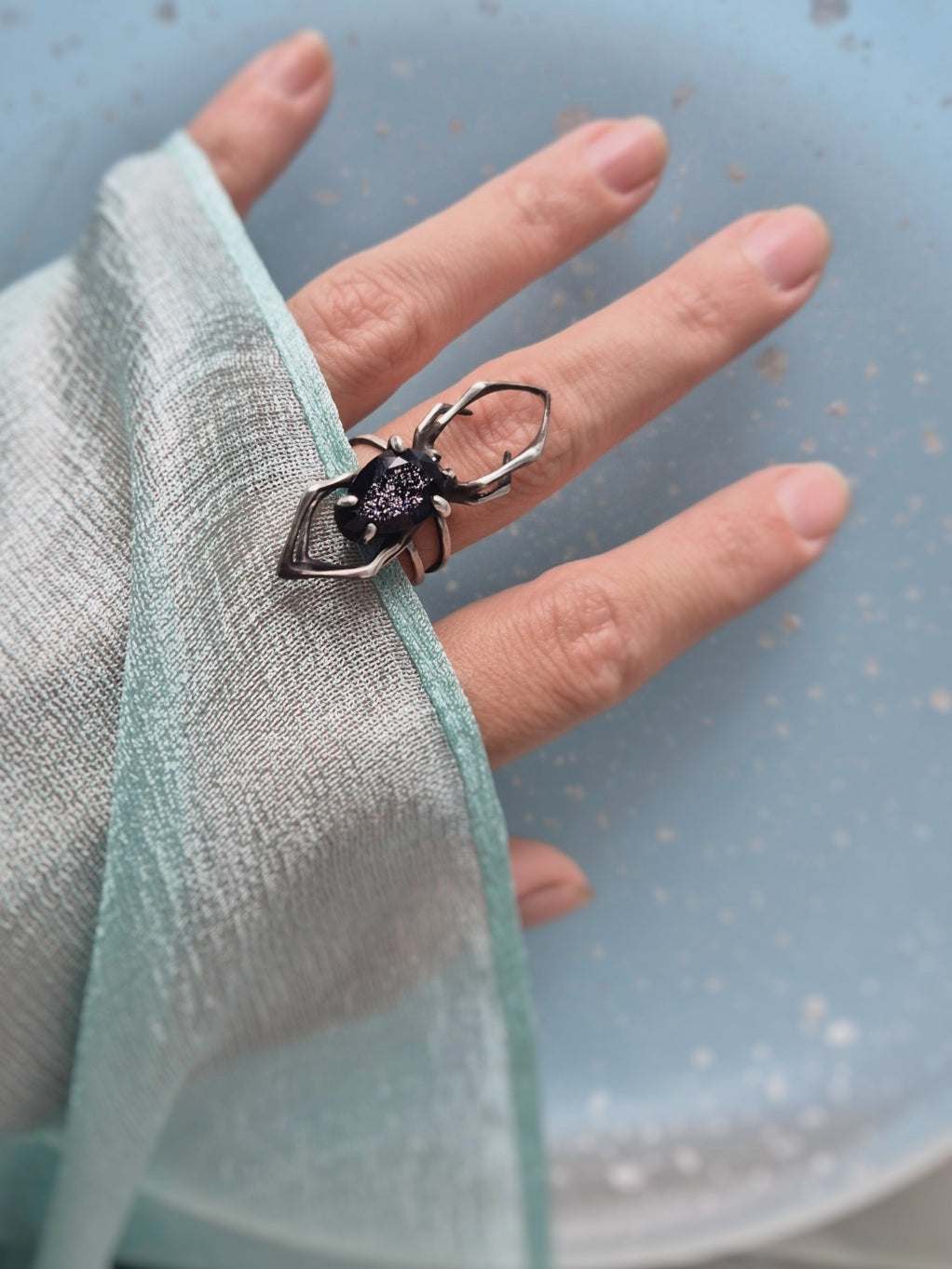 Silver spider ring worn on finger, paired with a mint green silk scarf sleeve