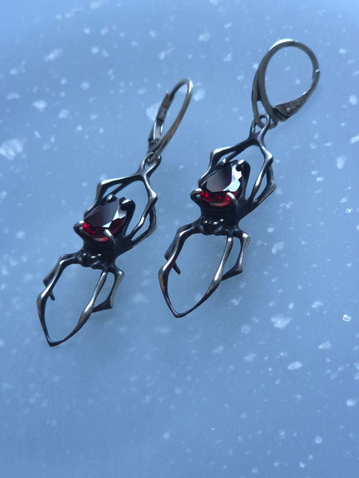 Macro shot of handmade oxidized silver spider earrings in the shape of spiders, set with polished garnets.