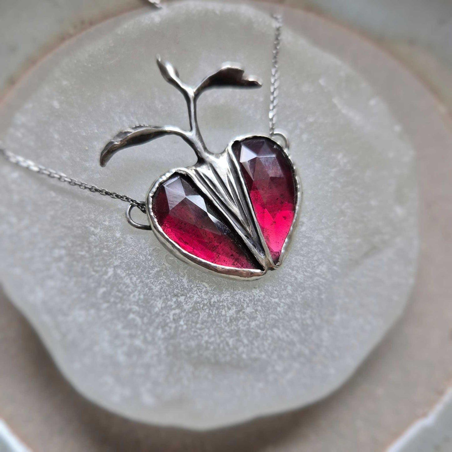 Side view of Seed Heart necklace with deep red garnets, catching light and revealing the texture of the silver setting.
