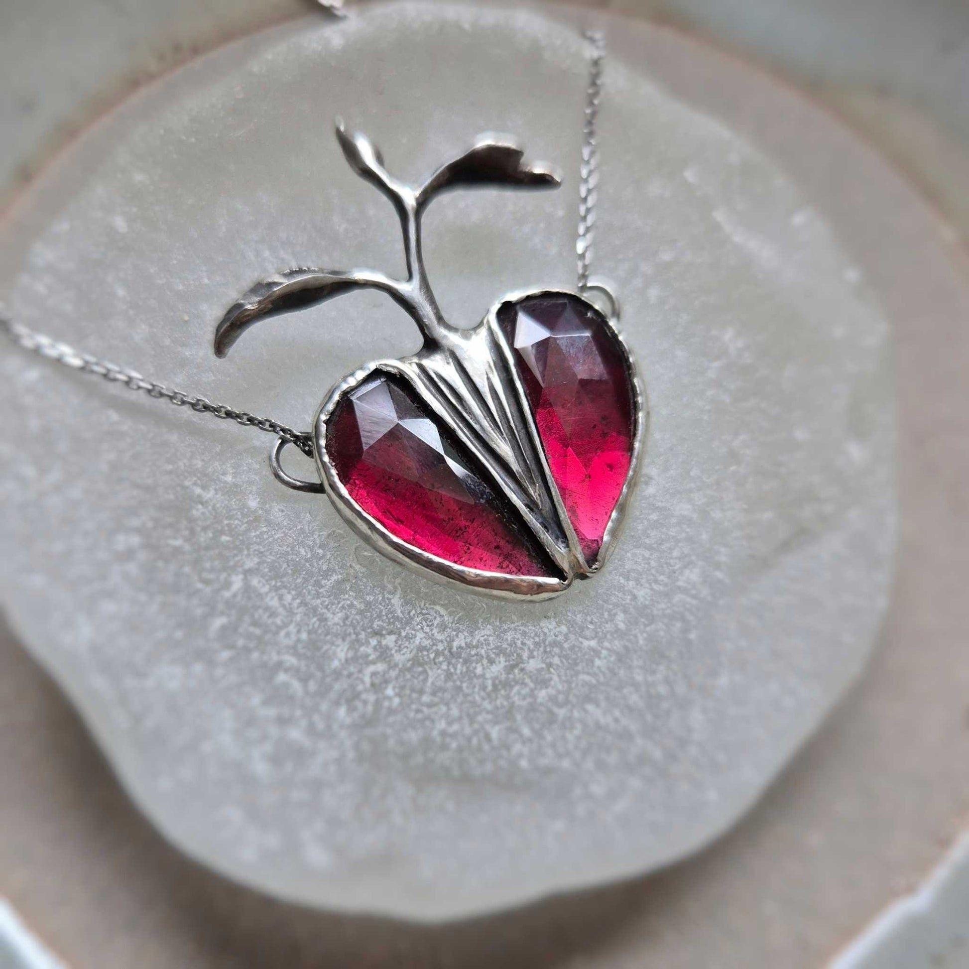 Side view of Seed Heart necklace with deep red garnets, catching light and revealing the texture of the silver setting.