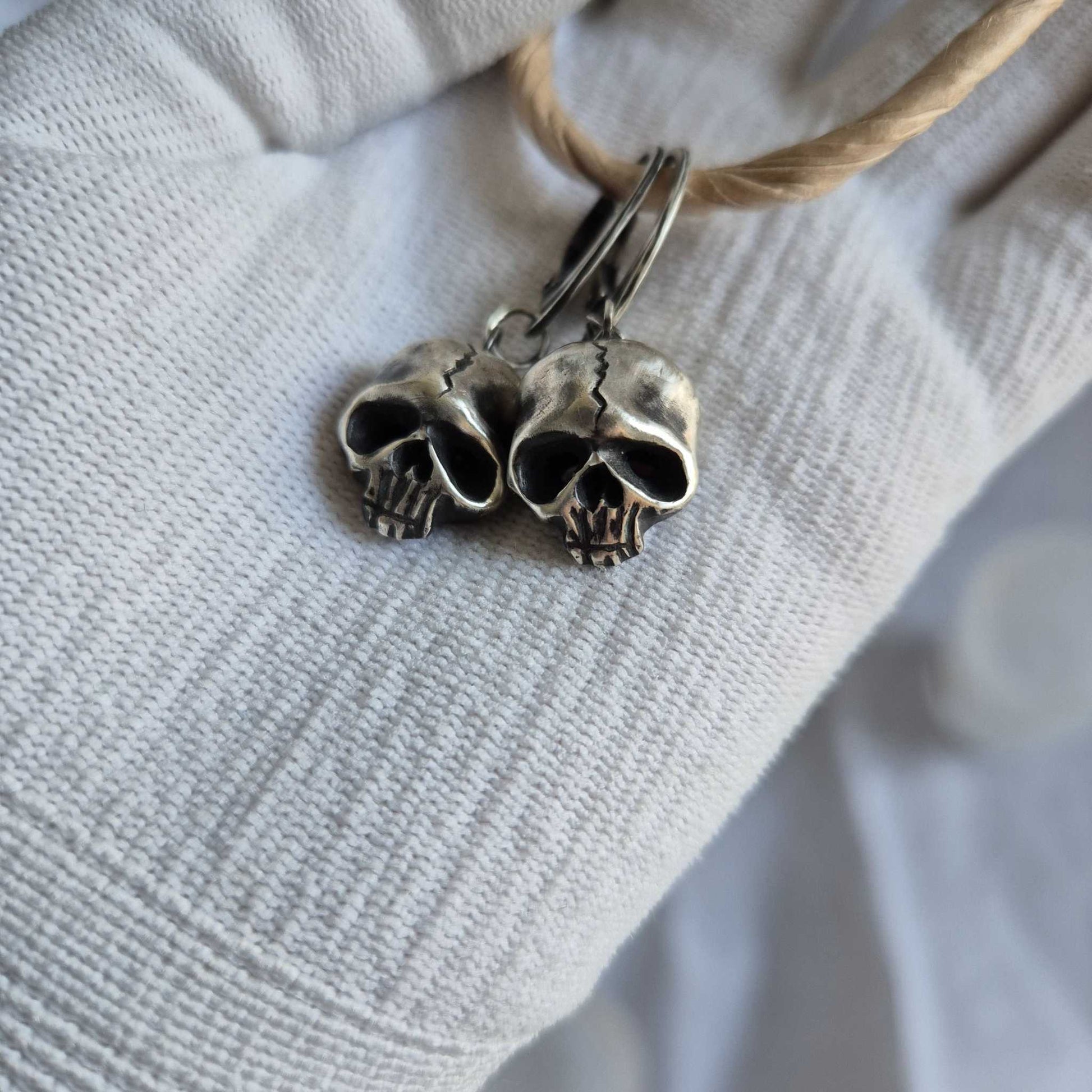 Close view of silver Skull earrings showing their expressive, miniature anatomy, in gloved hand